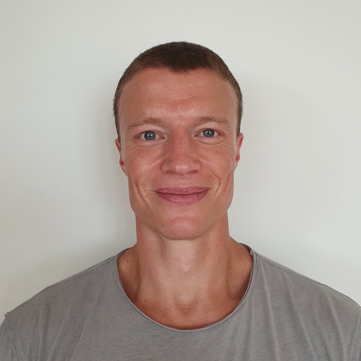 A person with short hair wearing a gray t-shirt smiling at the camera against a plain white background.