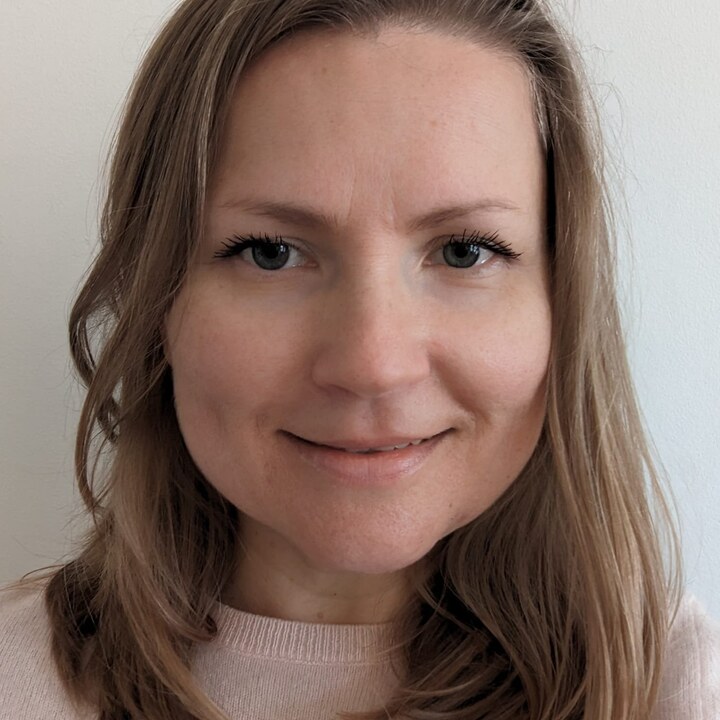 Portrait of a person with shoulder-length hair and a light pink sweater, smiling at the camera.