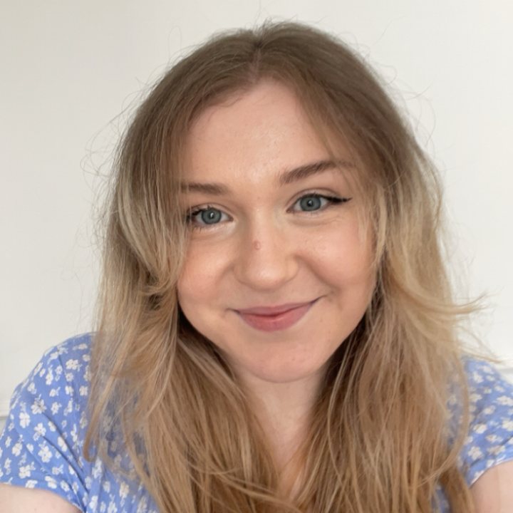 Smiling person with long hair wearing a patterned blue top, against a neutral background.