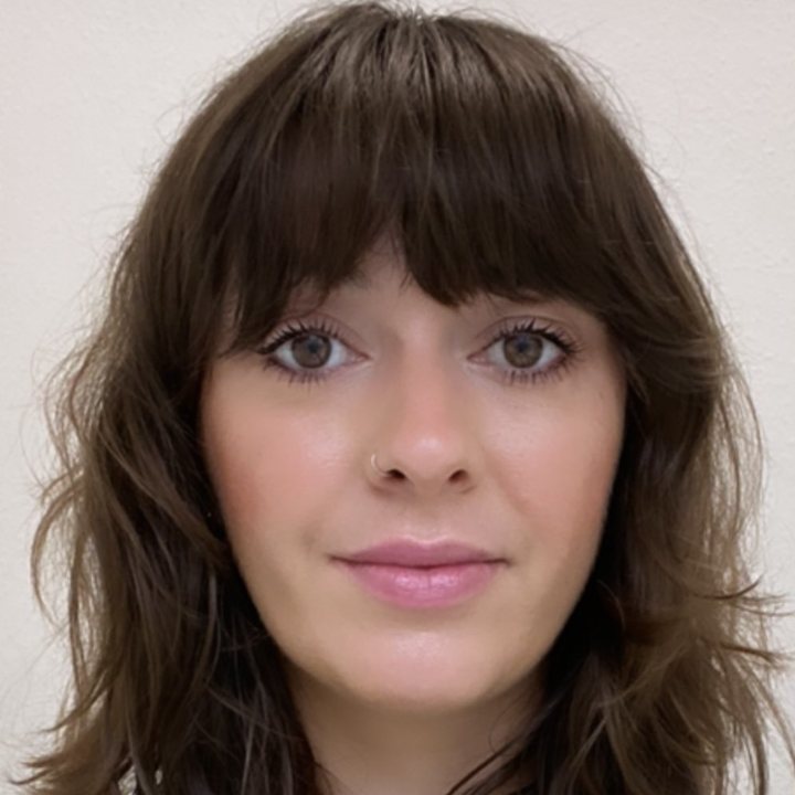 Person with long brown hair, wearing a green and white sweater, looking at the camera.